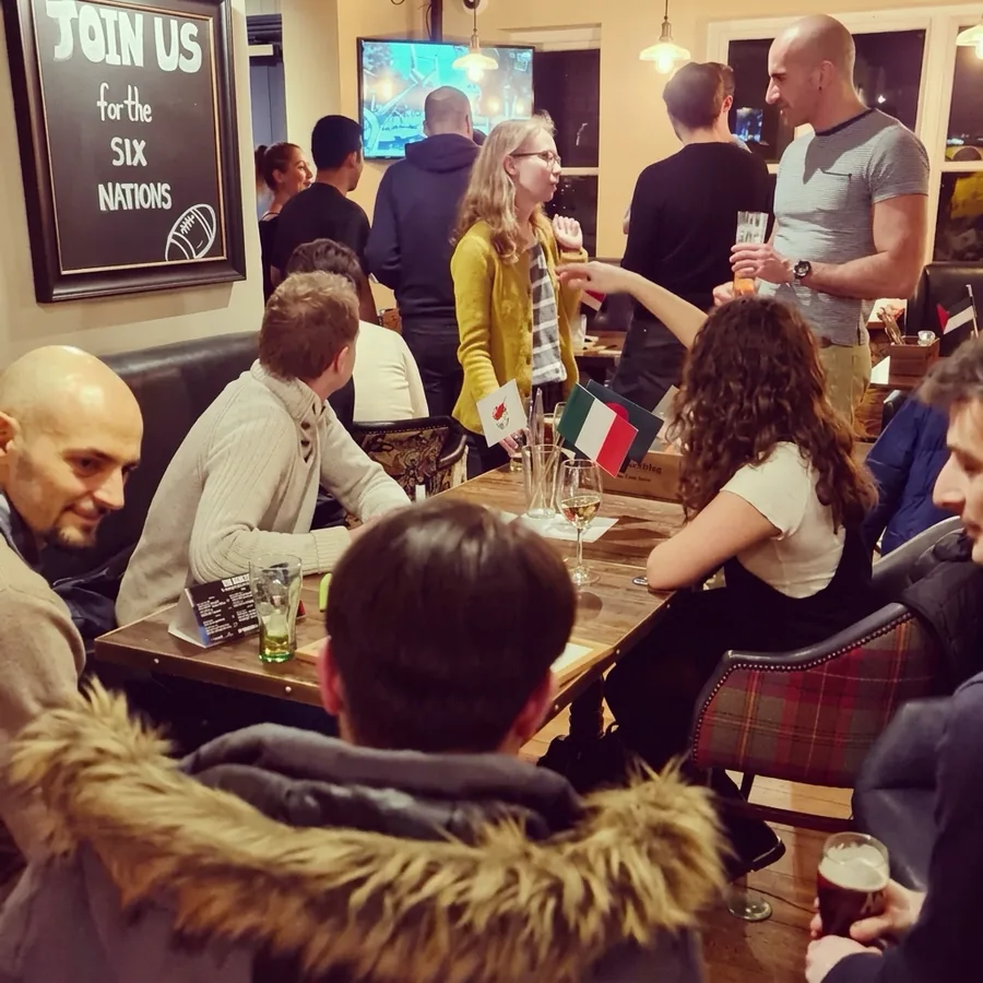 People chatting across tables with flags at a busy Guildford Babel evening